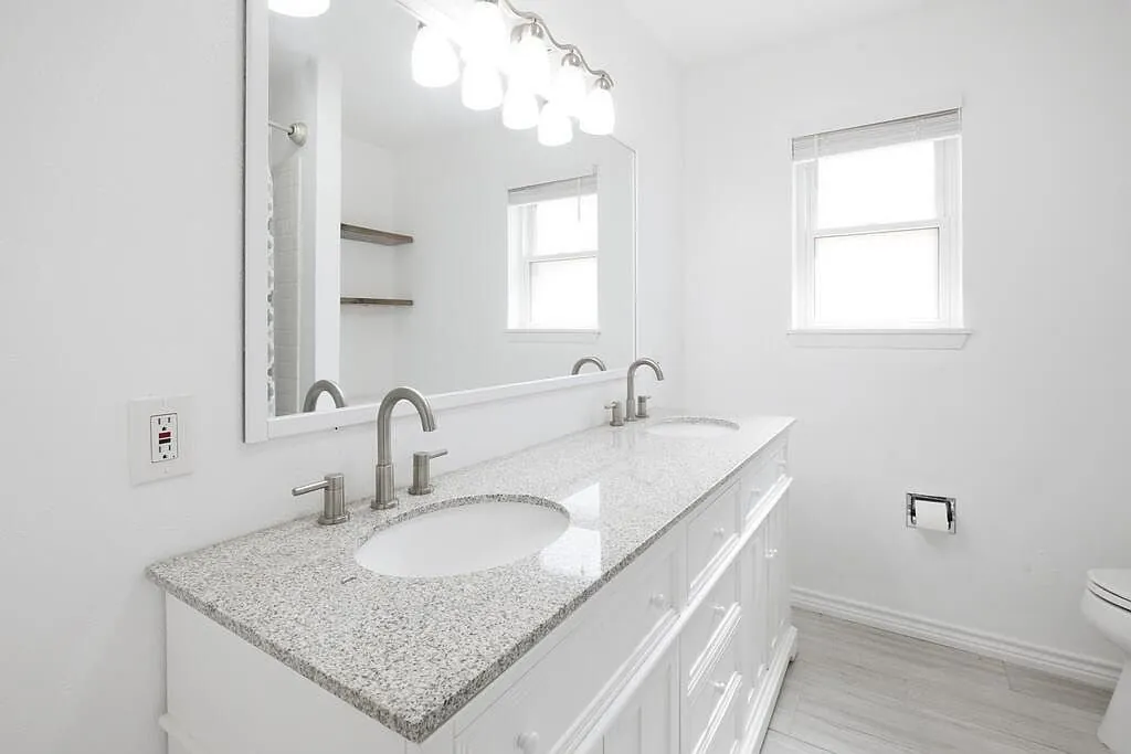 Bathroom after the remodel, with a granite double vanity and bright white finishes