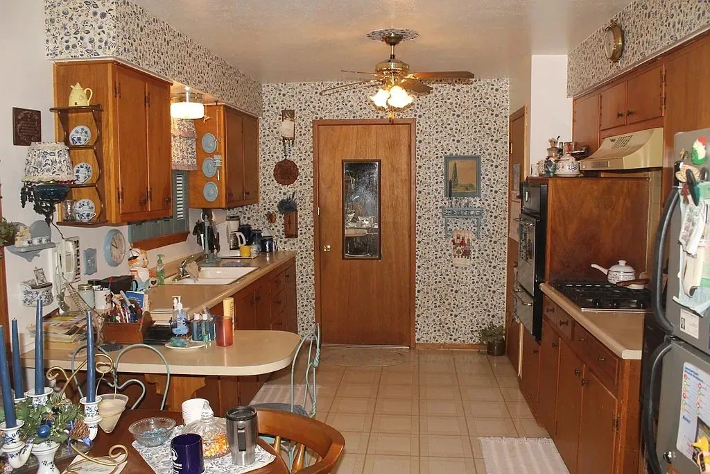 Kitchen before the remodel, with dated wood cabinets and patterned wallpaper