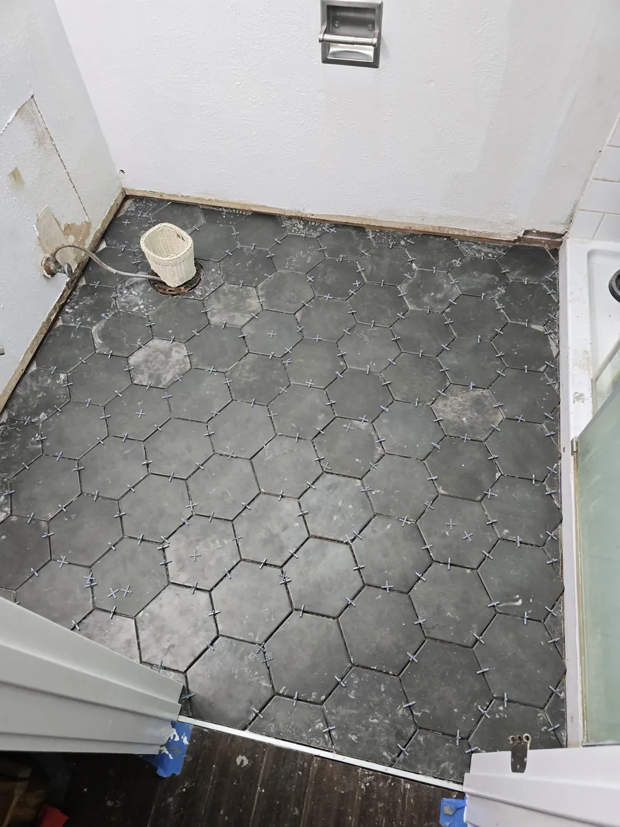 Large black hexagon floor tile laid with spacers in a bathroom, before grout